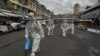 Workers wearing personal protective equipment (PPE) carry disinfectant to be sprayed at the Orussey market, after it was temporarily closed following a few vendors testing positive for the Covid-19 coronavirus, in Phnom Penh on April 4, 2021. (Photo by TANG CHHIN Sothy / AFP)