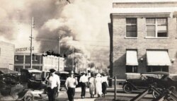 FILE - In this photo provided by the McFarlin Library at the University of Tulsa, two armed men walk away from burning buildings as others walk in the opposite direction, during the Tulsa Race Massacre, June 1, 1921, in Tulsa, Oklahoma.