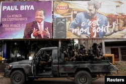 Cameroonian elite Rapid Intervention Battalion (BIR) members sit on their military vehicle under a plazard (L) of Cameroon President Paul Biya, who is running for re-election scheduled for Oct. 7, during a patrol in the south west city of Buea, Cameroon, October 4, 2018.