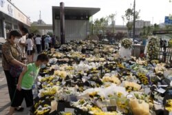 Orang-orang berdiri di samping bunga yang ditempatkan di pintu masuk stasiun kereta bawah tanah Metro Line 5 untuk mengenang korban banjir yang dipicu oleh hujan deras di Zhengzhou, provinsi Henan, China, 27 Juli 2021. (China Daily via REUTERS)