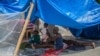 A woman and kids rest in the shade at a camp for people who lost their home during the August 14 earthquake in Les Cayes, Haiti, on August 23, 2021.