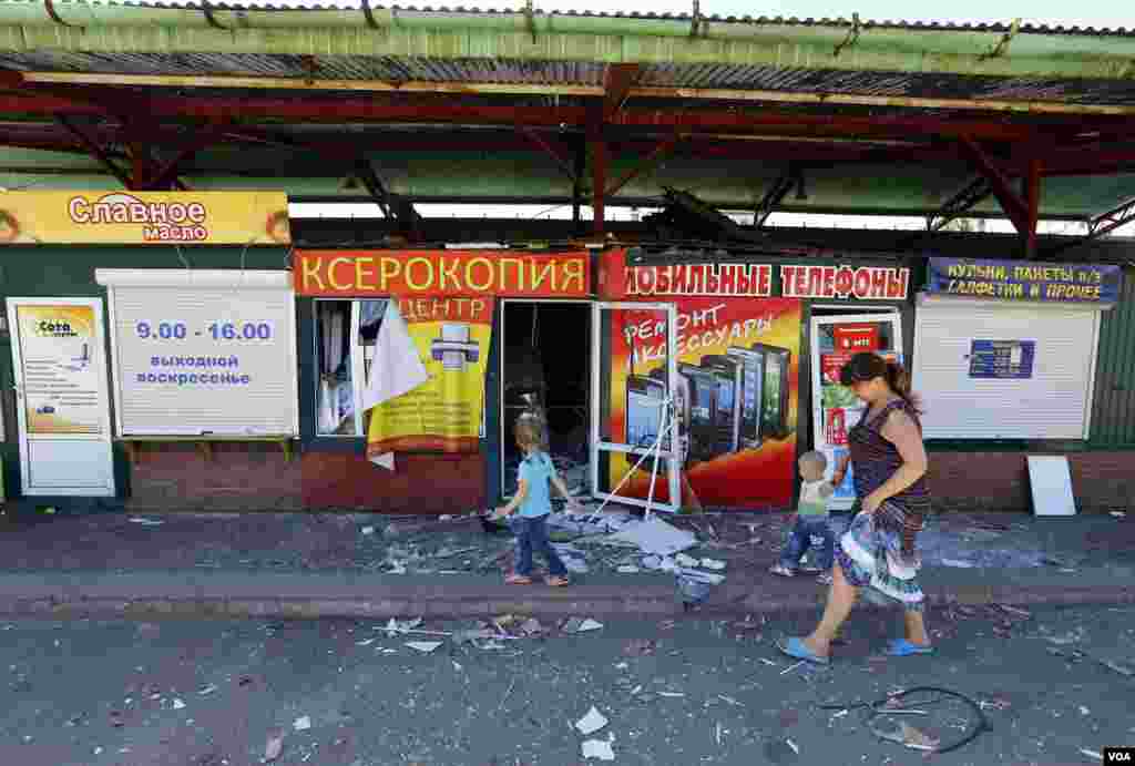 A woman and children walk past a damaged street market in the Ukrainian eastern city of Slovyansk, July 1, 2014.