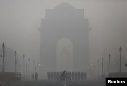 A man rides his bicycle next to Indian soldiers marching in front of India Gate on a smoggy morning in New Delhi, India, December 1, 2015.