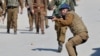 FILE - An Indian police officer aims his pellet gun towards demonstrators during a protest after Friday prayers in Srinagar, March 5, 2021. 