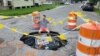 New Orleanian Joe Frisard sits beside a massive pothole two blocks from his home. Residents are no strangers to potholes, often decorating them or making jokes -- as was the case when someone placed a miniature car inside this one. (Matt Haines/VOA) 