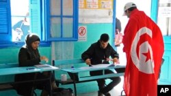 FILE - A Tunisian draped in the national flag arrives at a polling station to vote in La Marsa, outskirts of Tunis, Tunisia, Dec, 21, 2014.
