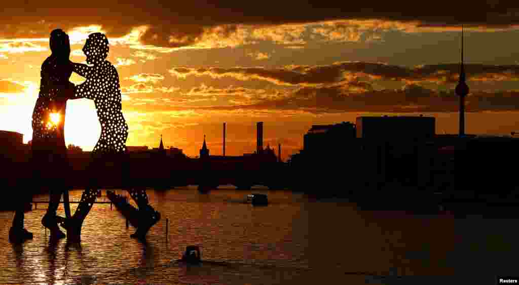 The sun sets behind the cityscape and the "Molecule Men", a 30-meter-high sculpture by Jonathan Borofsky, located in Berlin's Spree river, Germany, Aug.7, 2016.