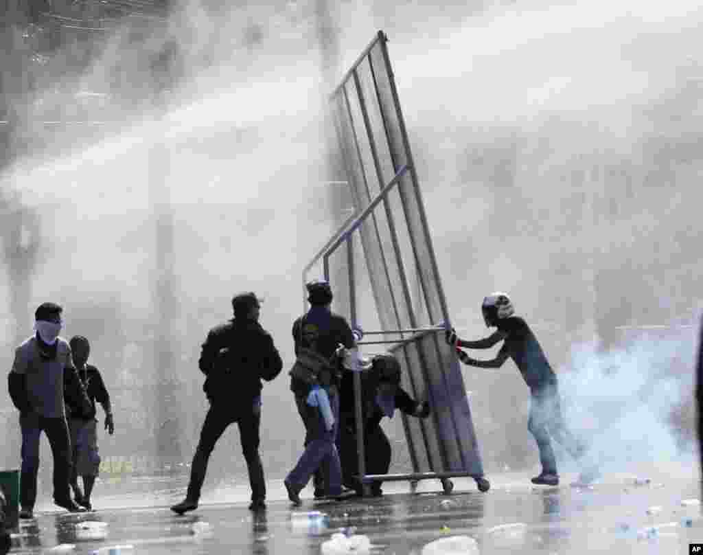 Para demonstran anti-pemerintah membentuk barikade melawan meriam air dan gas air mata yang ditembakkan oleh polisi anti huru-hara di Bangkok.