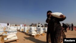 FILE - A displaced woman, who fled Mosul due to Islamic State violence, carries food in Khazer refugee camp, east of Mosul, Iraq, Nov. 7, 2016. 