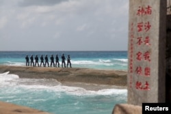 FILE - Soldiers of China's People's Liberation Army (PLA) Navy patrol near a sign in the Spratly Islands, known in China as the Nansha Islands, February 9, 2016. The sign reads "Nansha is our national land, sacred and inviolable."