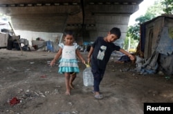 FILE - Children carry a drinking water container after filling it from a municipal tap under a flyover at a slum area in Kolkata, India, May 26, 2016.
