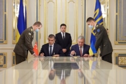 Ukraine's President Volodymyr Zelenskiy looks on while Defense Minister Andriy Taran and CEO of the Turkish defense technology company Baykar Haluk Bayraktar sign a memorandum to establish joint training and maintenance centers for Turkish armed drones, in Kyiv, Sept. 29, 2021.