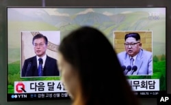 A visitor walks by a TV screen showing file footage of South Korean President Moon Jae-in, left, and North Korean leader Kim Jong Un, right, during a news program at the Seoul Railway Station in Seoul, South Korea, March 29, 2018.