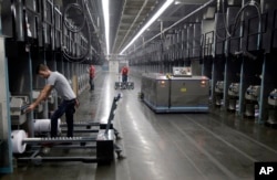 Para pekerja mengganti gulungan benang saat robot mengambil benang yang terbuat dari botol plastik daur ulang di perusahaan tekstil di Yadkinville, North Carolina.