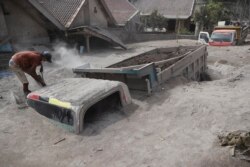 Seorang pria memeriksa truk yang tertimbun abu pasca erupsi Gunung Semeru di Kabupaten Lumajang, Jawa Timur, Minggu, 5 Desember 2021. (Foto: AP)