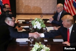 U.S. President Donald Trump and North Korea's leader Kim Jong Un shake hands during an expanded bilateral meeting at the Capella Hotel on the resort island of Sentosa, Singapore, June 12, 2018. With them are Senior North Korean Diplomat Ri Su Yong, top left, and White House Chief of Staff John Kelly, top right.