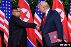 U.S. President Donald Trump and North Korea's leader Kim Jong Un shake hands during the signing of a document after their summit at the Capella Hotel on Sentosa island in Singapore, June 12, 2018.