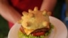 Pemilik restoran Hoang Tung memperlihatkan "burger corona" di Hanoi, Vietnam pada hari Rabu, 25 Maret 2020. Saat ini dunia sedang berjuang melawan pandemi Covid-19. (Foto: AP)