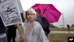 In a steady rain storm near the Washington Monument, Anastasia Bardin, 10, of New York City, left, with her mother Lyn Bardin, rallies with the Earth Action Team as part of Earth Day activities on the National Mall in Washington Sunday, April 22, 2012. 