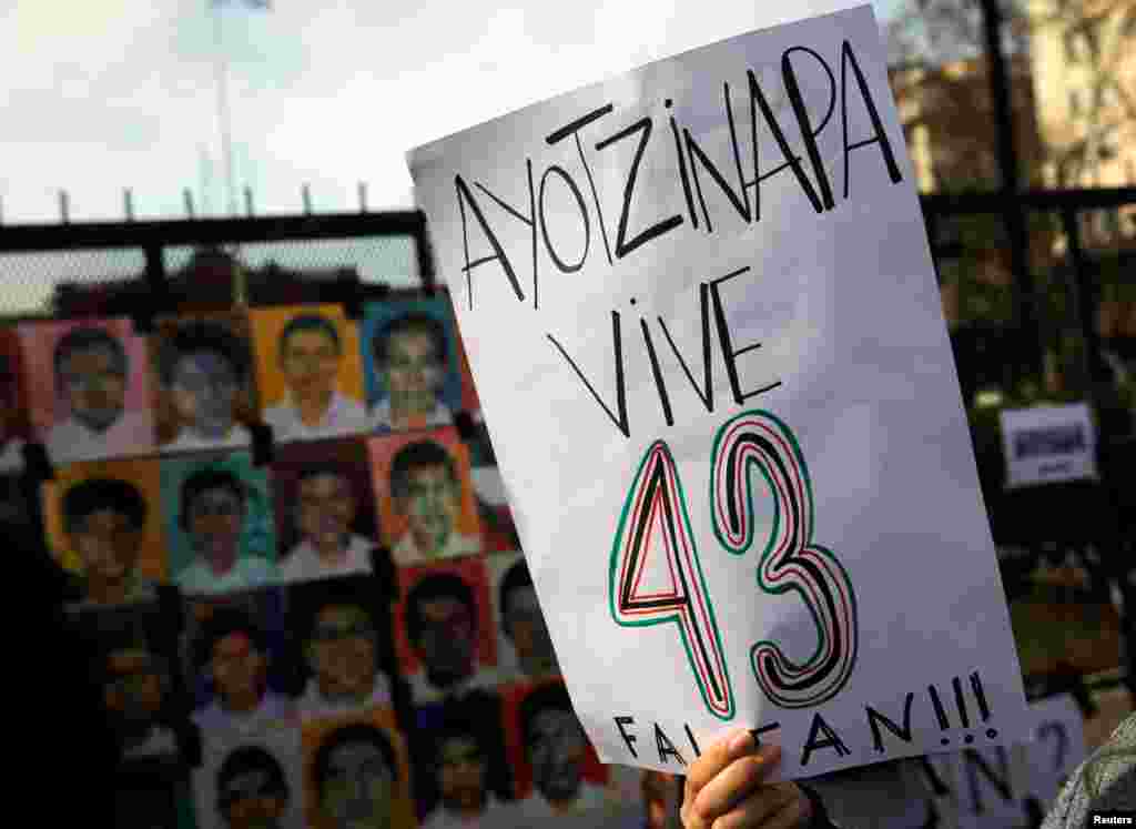 A woman holds up a sign that reads "Ayotzinapa lives - 43 are missing" next to pictures of the 43 missing students of Ayotzinapa College on a police fence outside the Casa Rosada Presidential Palace during a protest against the visit to Argentina by Mexico's President Enrique Pena Nieto, in Buenos Aires, Argentina.