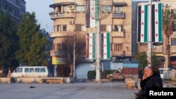 FILE - On Jan. 8, 2025 — about a month after the ouster of Syrian leader Bashar al-Assad — a man sits in Aleppo, Syria, near flags reflecting new leadership. Diplomats from around the world are pushing to stabilize Syria in the wake of Assad's fall. 