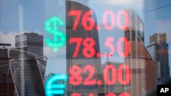 skyscrapers of the "Moscow City" are reflected in a glass window of an exchange office with the screen shows the currency exchange rate of the Russian ruble and U.S. dollar, Euro in Moscow, Russia, Tuesday, April 21, 2020. The Russian ruble fell Tuesday, driven down by a drop in oil prices. (Andrei Nikerichev, Moscow News Agency photo via AP)