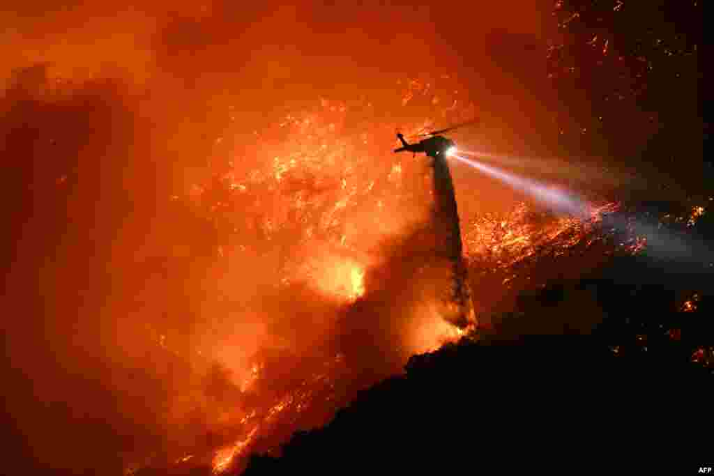 A fire fighting helicopter drops water as the Palisades fire grows near the Mandeville Canyon neighborhood and Encino, California, Jan. 11, 2025.