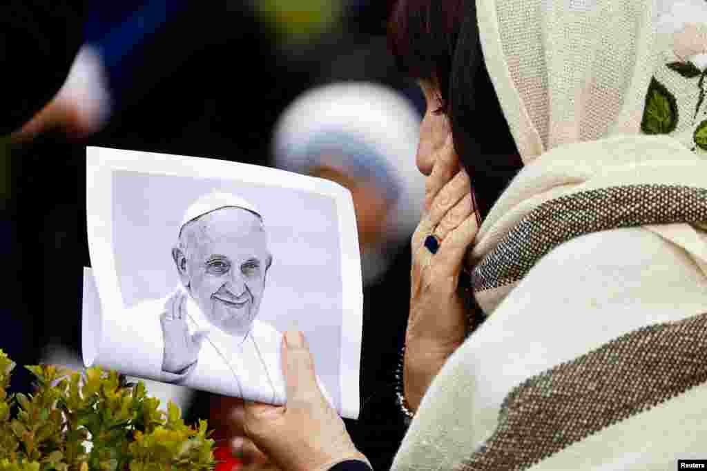 Seorang perempuan memegang gambar Paus Fransiskus di dekat patung mendiang Paus Yohanes Paulus II di luar Rumah Sakit Gemelli tempat Paus Fransiskus dirawat untuk melanjutkan perawatan, di Roma, Italia. (Reuters) 