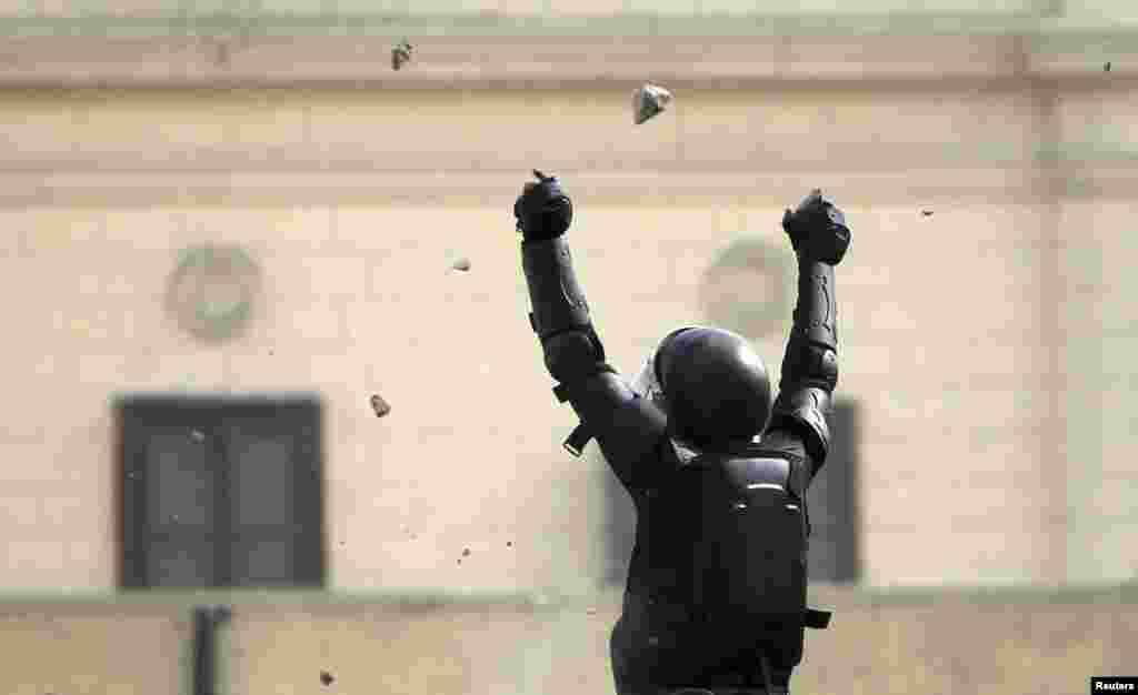 A riot police officer gestures during clashes with protesters opposing Egyptian President Mohamed Morsi throwing stones at him near Tahrir Square, Cairo, Egypt, January 25, 2013.