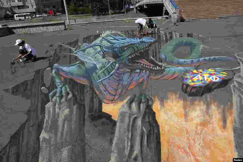 U.S. artist Tracy Lee Stum (L) and her assistants work on the "Singing Dragon" interactive 3-D street painting as they take part in the 4th Krasnoyarsk International Music Festival of the Asian-Pacific region in central Krasnoyarsk, Siberia, Russia.
