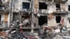 Petugas pemadam kebakaran bekerja di sebuah bangunan tempat tinggal yang rusak di Jalan Koshytsa, pinggiran Ibu Kota Ukraina Kyiv, di mana sebuah peluru militer diduga menghantam, pada 25 Februari 2022. (Foto: AFP)