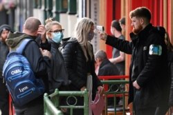 FILE - A security guard uses a handheld thermometer to take the temperature of customers, wearing face masks or coverings due to the COVID-19 pandemic, as they wait to enter a bar in Liverpool, England, Oct. 2, 2020.