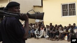 Un policier se tient devant des personnes accusées d’émeutes devant le tribunal de Kaduna, Nigeria, 20 avril 2011.