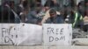 Seen through a wire fence, refugees and migrants most of them from Pakistan, hold placards during a third day of hunger strike to protest their deportation to Turkey, in the Greek island of Lesbos, April 7, 2016. 