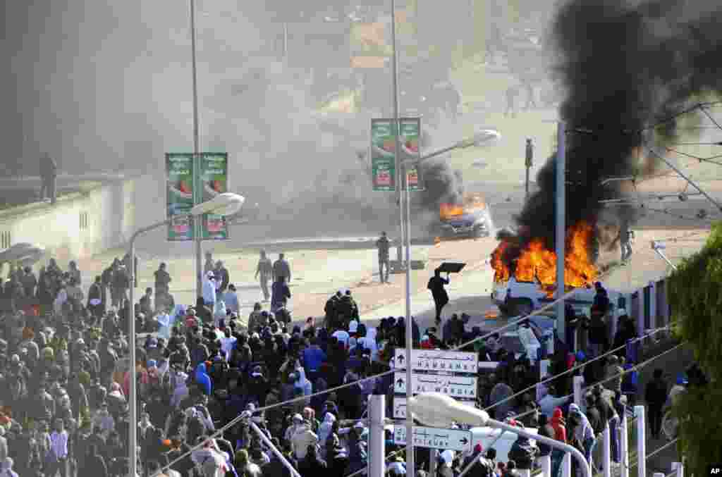 Mobil terbakar di samping pemakaman&nbsp;el Jallez di mana ribuan Tunisia yang berkumpul untuk menghadiri pemakaman pemimpin oposisi yang dibunuh, Shokri Belaid, dekat Tunis. 