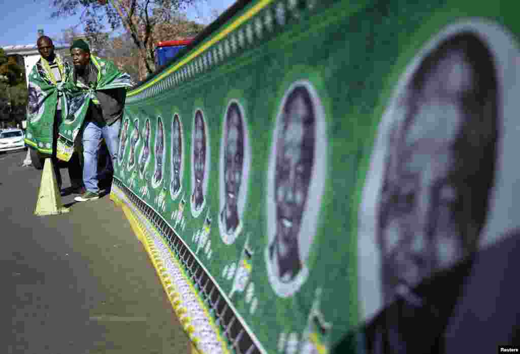 Men stand next to a banner covered with portraits of Nelson Mandela to a wall outside the Mediclinic Heart Hospital in Pretoria, June 28, 2013.