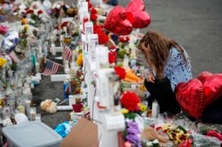FILE - Gloria Garces kneels in front of crosses at a makeshift memorial, Aug. 6, 2019, near the scene of a mass shooting in El Paso, Texas.