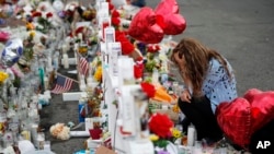 FILE - Gloria Garces kneels in front of crosses at a makeshift memorial near the scene of a mass shooting at a shopping complex, Aug. 6, 2019, in El Paso, Texas. 