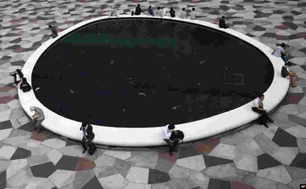 People take a rest around an artificial pond with images of carp at the bottom, in Tokyo, Japan.