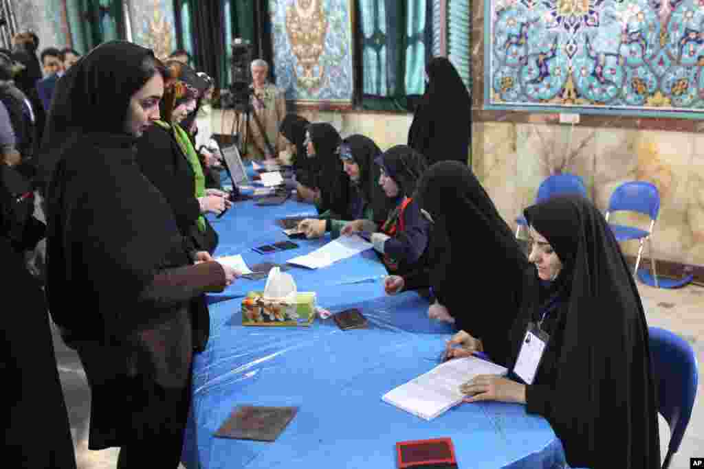 Iranian voters, left, arrive at a polling station to vote for their country's parliamentary and Experts Assembly elections as election staff receive them in Tehran, Iran, Feb. 26, 2016.