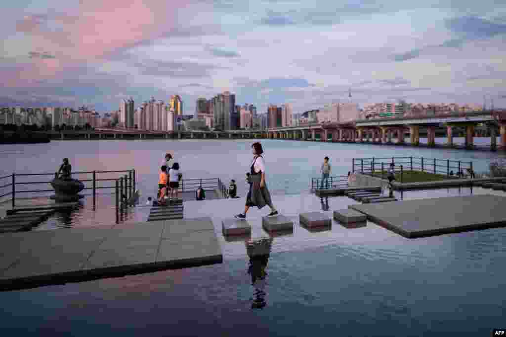 A woman walks over stepping-stones before the Han river and Seoul's skyline at Yeouido park, South Korea.