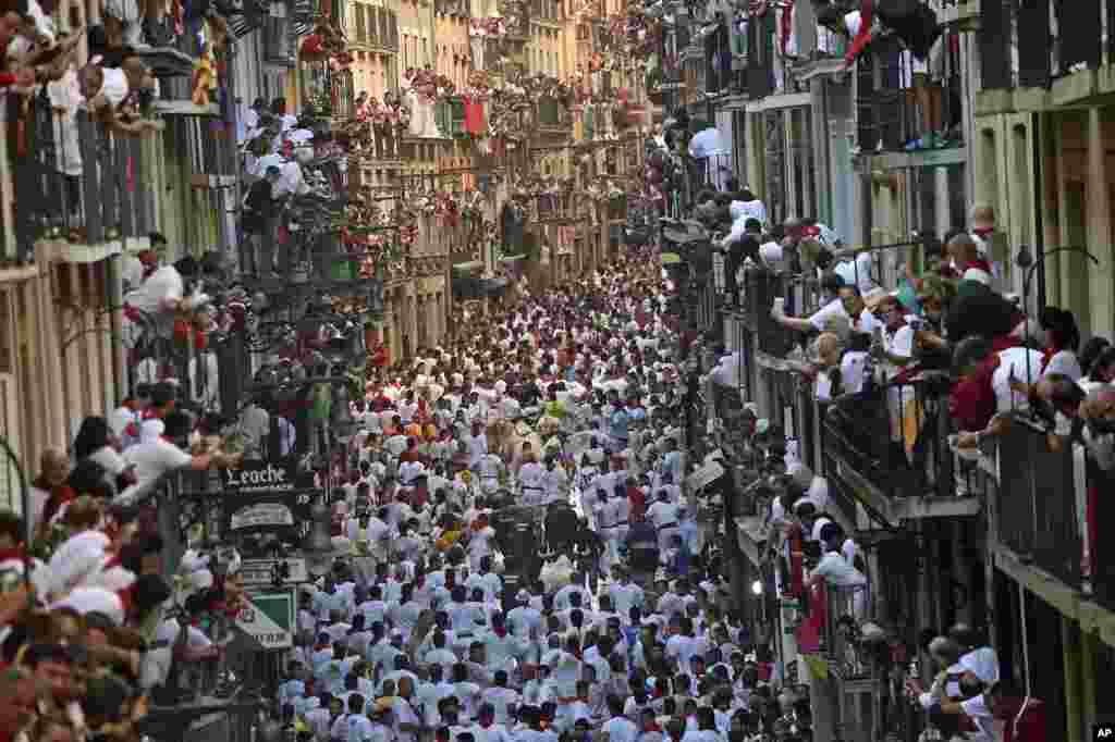 Revelers run on Estafeta street to stay ahead of charging bulls as people watch from balconies during the first running of the bulls at the San Fermin Festival, in Pamplona, Spain.
