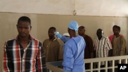 FILE - A health worker, center, takes the temperature of people to see if they might be infected by the Ebola virus inside the Ignace Deen government hospital in Conakry, Guinea, March 18, 2016.