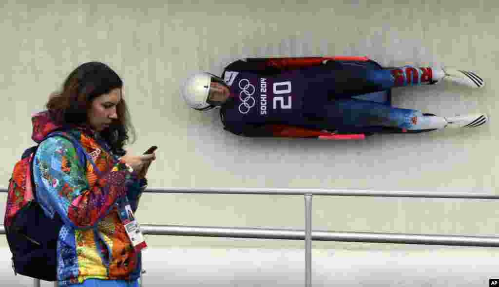 Natalja Khoreva of Russia takes a turn as a volunteer looks at her cell phone during the women's singles luge training, Krasnaya Polyana, Russia Feb. 9, 2014.