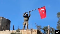 Seorang tentara mengibarkan bendera Turki pada saat pasukan Turki merebut bukit Bursayah, yang memisahkan Afrin, daerah kantong kekuasaan Kurdi dan Kota Azaz di Suriah, yang dikuasai Turki, 28 Januari 2018. 