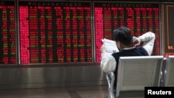 An investor reads a newspaper in front of electronic board showing stock information at a brokerage house in Beijing, China, Oct. 29, 2015. 