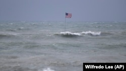 Bendera AS berkibar dari sebuah kapal yang karam di tengah gelombang pasang dari Badai Tropis Isaias, di Vero Beach, Florida, Minggu, 2 Agustus 2020. 