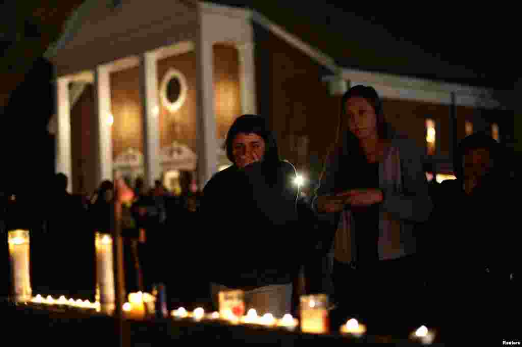 Seorang wanita menutup mulutnya saat pelayat lainnya memandangi lilin-lilin yang dipajang di luar gereja Katholik Santa Rosa dari Lima dekat SD Sandy Hook, Newtown, Connecticut, tempat terjadinya tragedi penembakan massal hari Jum'at tanggal 14 Desember 2012.
