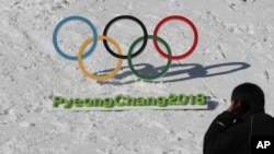 Un homme passe devant les anneaux olympiques avec un signe des Jeux olympiques d'hiver 2018 de Pyeongchang à Pyeongchang, en Corée du Sud, 3 février 2017.