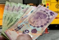 FILE - A man shows Argentine pesos outside a bank in Buenos Aires' financial district, Argentina, Aug. 30, 2018.